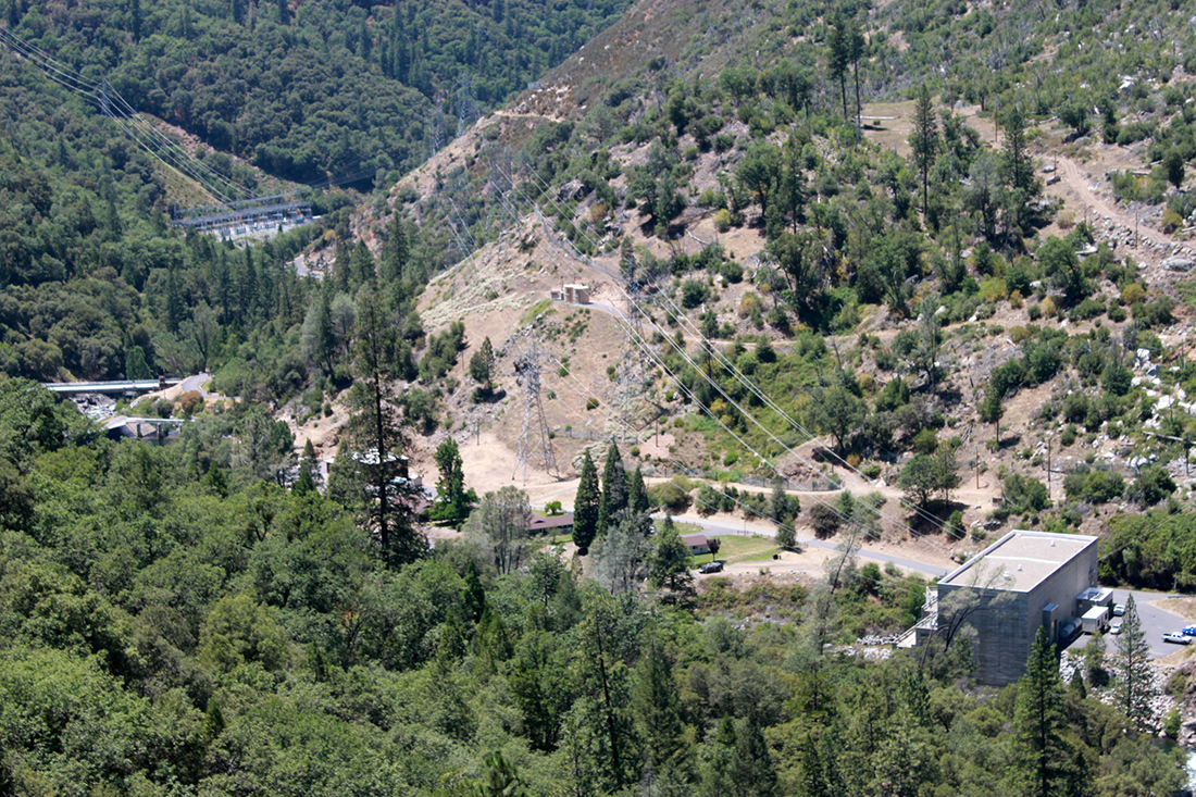 a utility building, transmission lines, and a substation at the bottom of a steep canyon, viewed from above