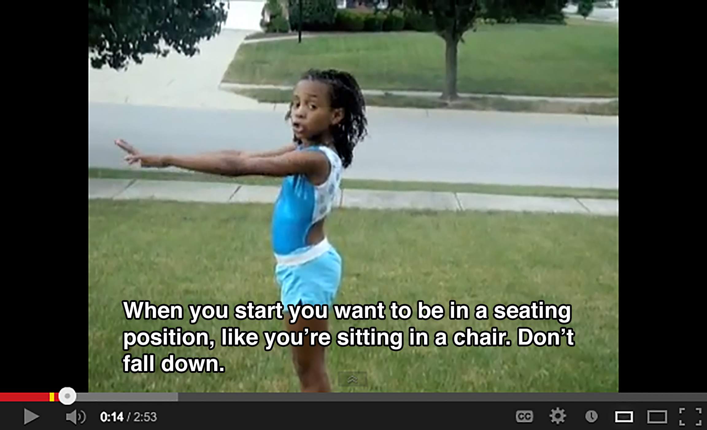 A young girl stands in a yard with her arms stretched outward and says: When you start you want to be in a seating positions, like you're sitting in a chair. Don't fall down.